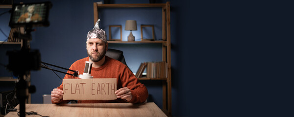 Strange bearded man vlogger in foil hat showing Flat Earth banner speaking with his subscribers on...