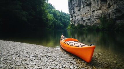 A vibrant orange kayak rests on a rocky shore by a calm river surrounded by lush green cliffs.