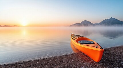A vibrant orange kayak rests by a tranquil lake at sunrise, with misty mountains reflecting in the calm water.