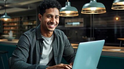 Smiling young man working on laptop in modern workspace with warm lighting and bookshelves
