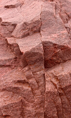 Structure of uneven layered surface of rough red granite with quartz inclusions. Colored granite texture vertical image