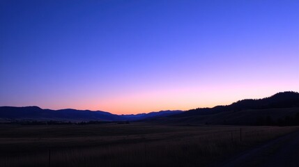 Fototapeta premium A serene twilight landscape with mountains and a vast field under a gradient sky.
