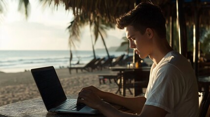 A young man works on a laptop at a beachside table, surrounded by palm trees and ocean views during sunset.