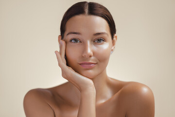 Close-up of a woman with clear skin posing thoughtfully, resting her face on her hand against a...