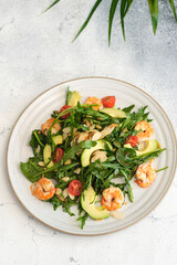 Top view of a gourmet shrimp salad served with fresh vegetables, avocado slices, and almond flakes on a rustic plate.