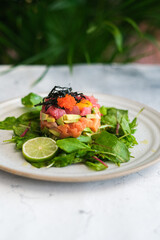 Close-up shot of an elegantly arranged tuna tartare tower with layers of fresh avocado, diced tuna, and a topping of vibrant tobiko and seaweed, served with a side of fresh lime.