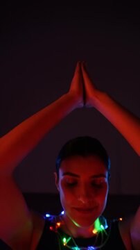 Woman meditating in a Christmas atmosphere with yf garlands on her body. Christmas yoga. Christmas concept. Vertical video 4k