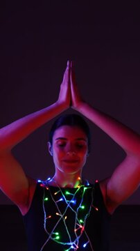 Woman meditating in a Christmas atmosphere with yf garlands on her body. Christmas yoga. Christmas concept. Vertical video 4k