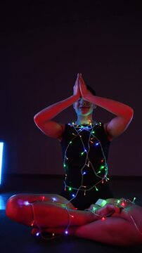 Woman meditating in a Christmas atmosphere with yf garlands on her body. Christmas yoga. Christmas concept. Vertical video 4k