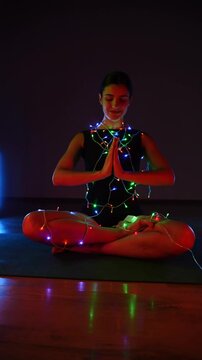 Woman meditating in a Christmas atmosphere with yf garlands on her body. Christmas yoga. Christmas concept. Vertical video 4k