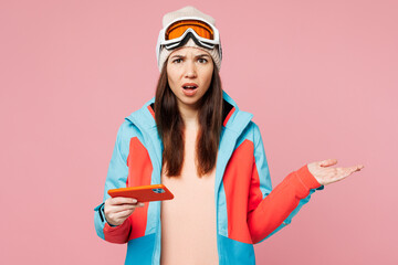 Skier young woman wear warm blue padded jacket ski goggles mask spend extreme weekend winter season in mountains play racing app on mobile cell phone isolated on plain pink background. Hobby concept. © ViDi Studio