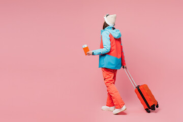 Back view traveler woman wear blue padded jacket ski goggles mask hold passport ticket bag isolated on plain pink background Tourist travel abroad in free time getaway Air flight trip journey concept