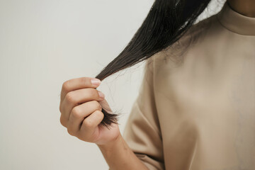 Naklejka premium Close up of a hand holding a strand of black hair against a white background