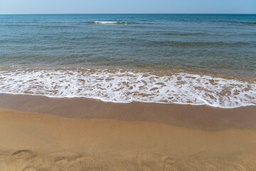 Emerald-blue transparent sea water washes yellowish sand. White waves rolls on sandy shore of Black Sea Anapa. White splashes and foam in foreground. Sea at southern resort of Russia.