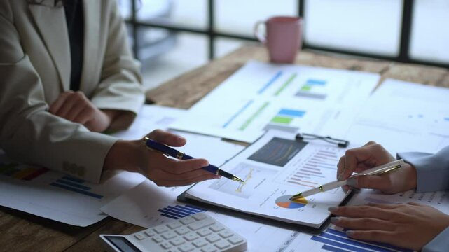 Two people are looking at a table with a lot of papers and a calculator. They are discussing something important