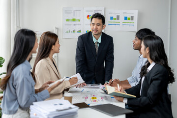 A group of people are sitting around a table with papers and graphs