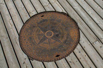 Old rusty compass on a wooden deck in a park, closeup of photo. unusual well hatch