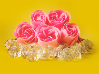 Pink rose petals on acrylic gem stones, yellow color background. Abstract floral background.