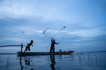 Fisherman casting his net at sunrise. Silhouette Asian fisherman on wooden boat casting a net in the Lake. Vietnamese Fisherman throwing net.