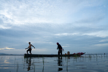 Fototapeta premium Fisherman casting his net at sunrise. Silhouette Asian fisherman on wooden boat casting a net in the Lake. Vietnamese Fisherman throwing net.