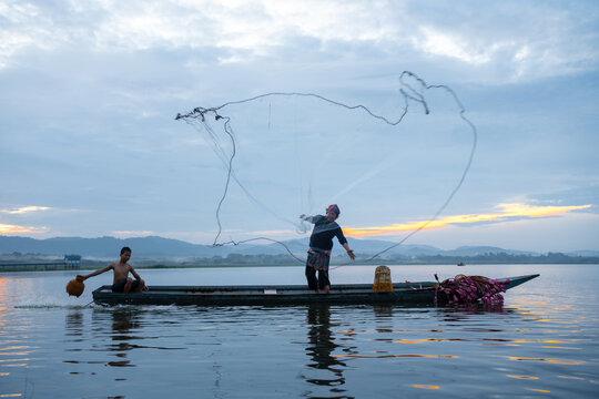 Fisherman casting his net at sunrise. Silhouette Asian fisherman on wooden boat casting a net in the Lake. Vietnamese Fisherman throwing net.