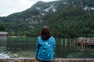 A young slender girl sits on a wooden pier with her back.