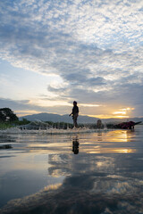 Fototapeta premium Fisherman casting his net at sunrise. Silhouette Asian fisherman on wooden boat casting a net in the Lake. Vietnamese Fisherman throwing net.