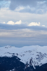 Snowy Alpine Peaks Under a Dramatic Cloudy Sky, Capturing the Rugged Beauty and Winter Serenity of the Mountainous Landscape in the Alps