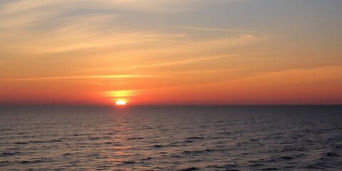 Obraz premium Breathtaking Orange and Yellow Sunset Over Calm Ocean Waves with Soft Clouds in the Evening Sky Illuminated by Golden Light
