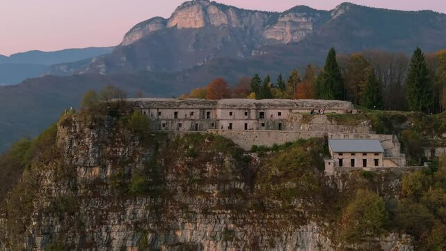A breathtaking aerial view showcasing Punta Corbin, a historic fortress in Northern Italy, surrounded by lush greenery and rugged mountainous terrain.
