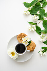 A cup of coffee, white saucer, oatmeal cookies, white roses and jasmine flowers. Mother's day card, valentine's day.