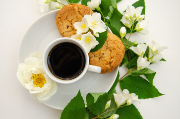 A cup of coffee, white saucer, oatmeal cookies, white roses and jasmine flowers. Mother's day card, valentine's day.