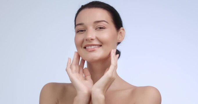 A beautiful young woman smiling with hands on her face, showcasing flawless skin. Perfect for skincare ads, natural beauty promotions, or wellness branding. Professional studio video.
