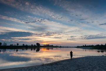 Matins landscape on a wide river. Summer. Sunrise. Photographer and tripod. Sandy beach. Reflection of clouds in the water