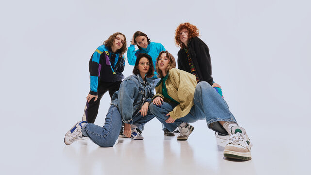 Stylish young people, two women and five men in their 20s, dressed in classic retro-inspired outfits and retro sneakers, posing against white studio background. Concept of 90s fashion, youth culture
