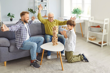 Grandfather, father, and son playing a board game together at home, celebrating a win. Family...