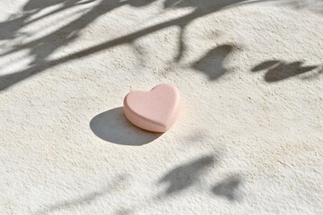 Obraz premium A pink heart-shaped object resting on a textured surface, casting soft shadows.