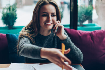 Positive smiling female economist calling friend using application on modern mobile phone in work...