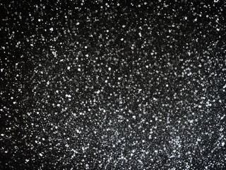 Glittery white texture on black background with confetti creates a sparkling abstract design