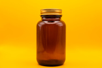 Amber glass jar with golden lid on yellow background