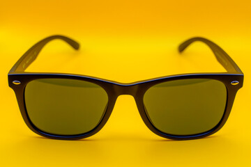 Stylish black sunglasses with green lenses on yellow backdrop