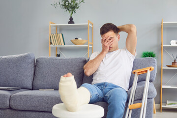 Man feeling bad pain, sad with broken leg or foot injury sitting with crutches, bandaged leg at...