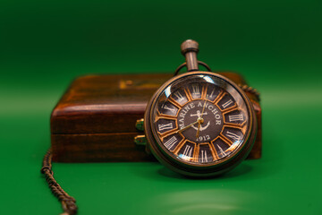 Vintage pocket watch with wooden box on green background