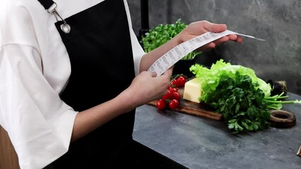 A chef reviews a shopping list in a modern kitchen, surrounded by vibrant vegetables and fresh herbs. The setting is lively, highlighting the joy of cooking with quality ingredients.