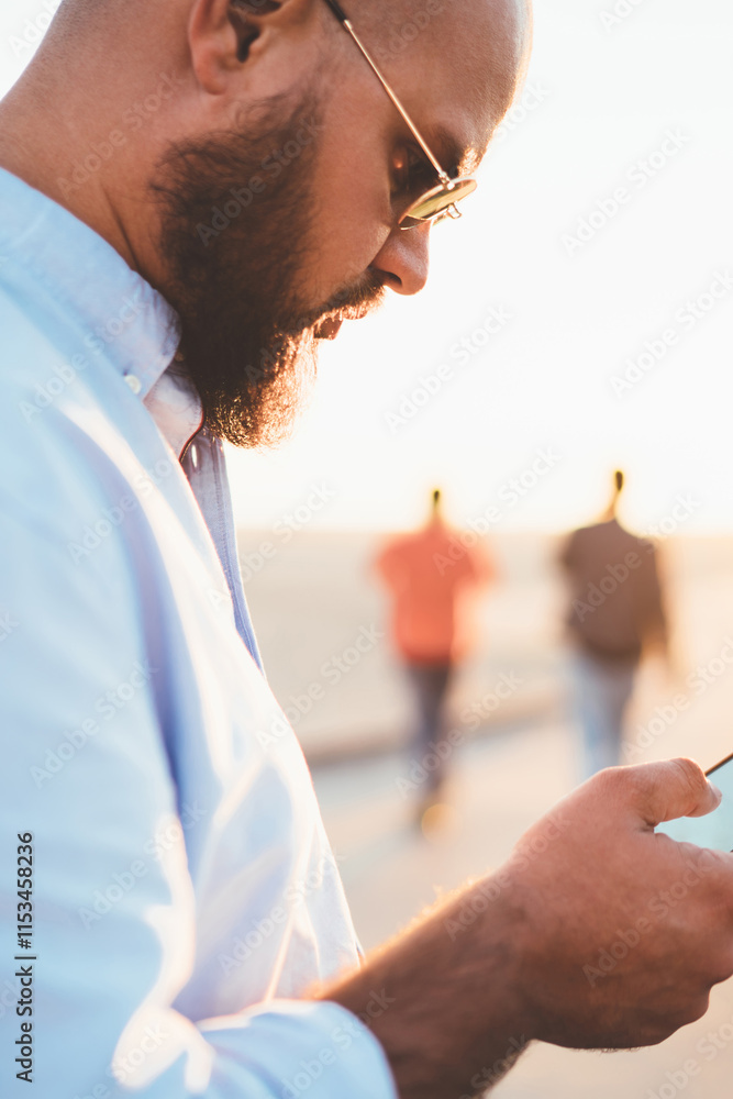 Poster young handsome guy holding smartphone making transaction via banking application standing on street,
