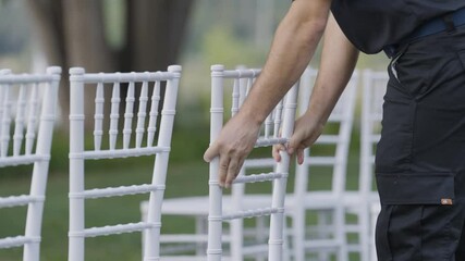 event planner organise move white chair in outdoor location with park garden tree in blurred background