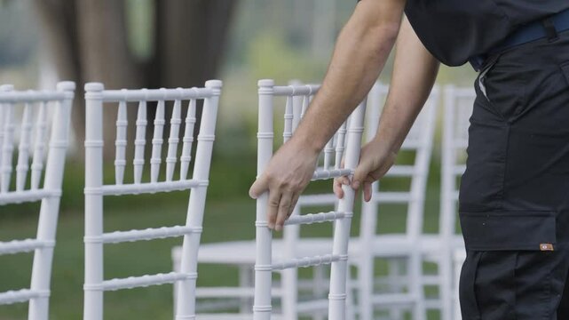 event planner organise move white chair in outdoor location with park garden tree in blurred background