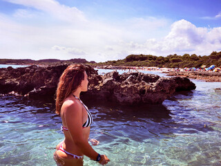 Gorgeous longhaired Caucasian girl in bikini bathing in crystal-clear water near the rocks. Ostuni, Apulia (Puglia), Italy.     