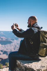 Young hipster guy enjoying beautiful landscape of National park taking picture on smartphone camera,male traveler photographing scenery nature view in Grand Canyon on high mountain cliff with cellular