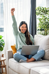 Pretty motivated woman celebrating something while working with laptop sitting on a couch at home